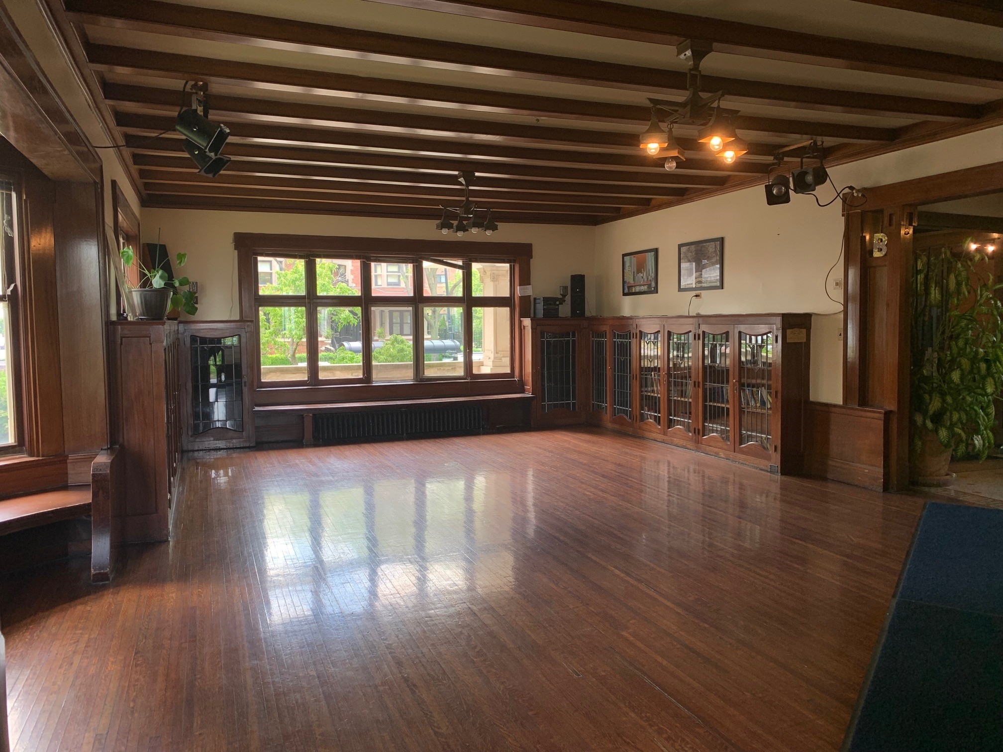 Empty room with dark wood beamed ceiling, hardwood floor, large windows, and built-in cabinets.